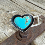 Silver bracelet with a turquoise heart-shaped stone on a rustic metal surface